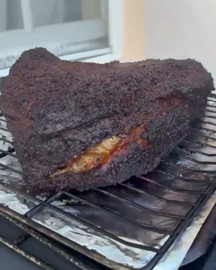 A whole bark-crusted smoked brisket resting on the grill grate