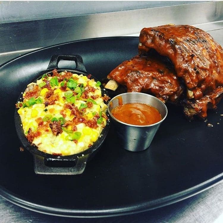 Sauced baby back ribs beside a skillet of creamed corn